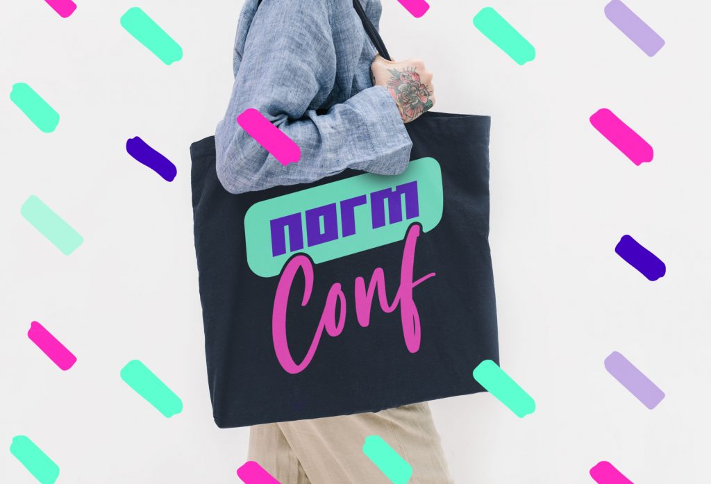 A person carrying a black tote bag with the NormConf logo
